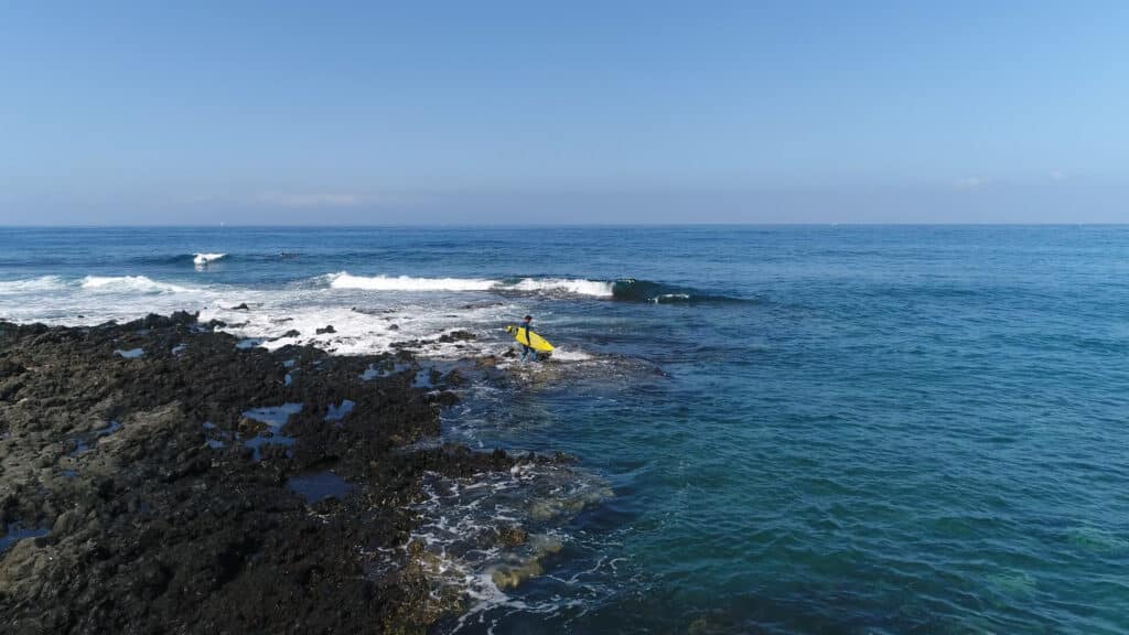 Surfista en las rocas de Punta Blanca entrando en el mar